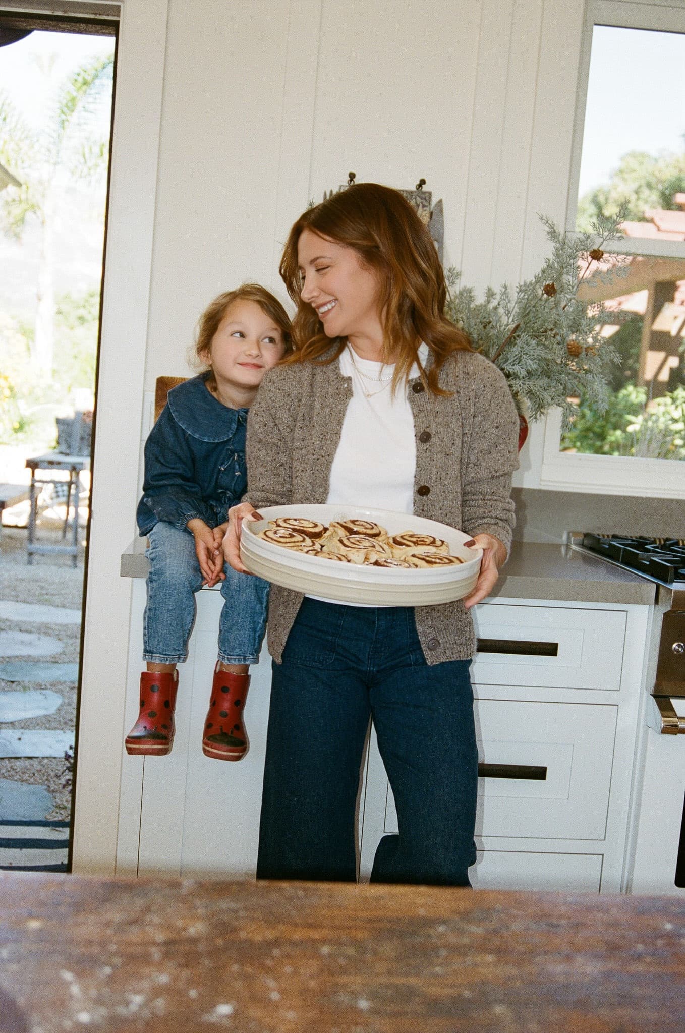 Woman holding a plate of cookies with a child in a kitchen.